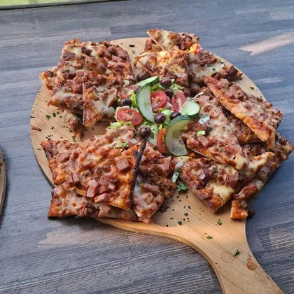 A thin-based loaded pizza on a board with a side salad