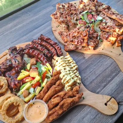 A loaded grill sharing board with ribs, wings and sides next to a pizza board